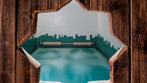 A swimming pool framed by wooden panels with a cityscape mosaic wall. - Historic Hotel La Stua (Cavalese)