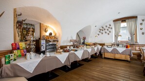A restaurant with multiple tables covered with white tablecloths, wooden flooring, and a variety of food and drink items displayed on the tables. - Historic Hotel La Stua (Cavalese)