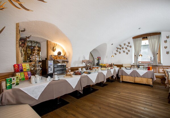 A restaurant with multiple tables covered with white tablecloths, wooden flooring, and a variety of food and drink items displayed on the tables. - Historic Hotel La Stua (Cavalese)