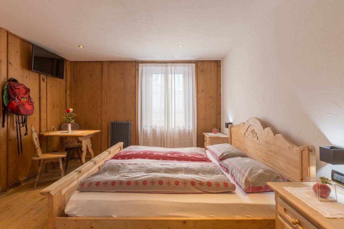 A wooden room with a bed, a desk, a chair, and a window with curtains.