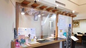 A reception desk with informational posters, a clear plastic barrier, and a wooden ceiling structure. - Hotel Select Inn Nagano (Nagano)