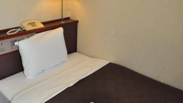 A hotel room with a bed, a bedside lamp, a telephone, and a folded towel on the floor.
