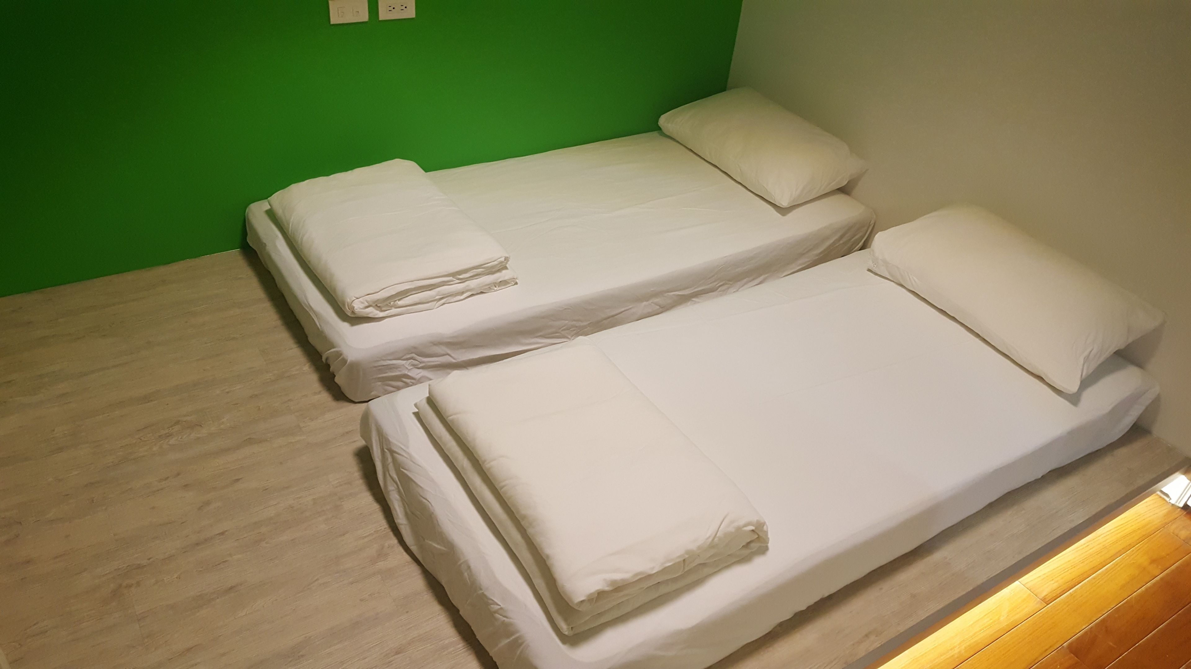 Dos camas individuales con ropa de cama blanca en una habitación con paredes verdes y suelo de madera.