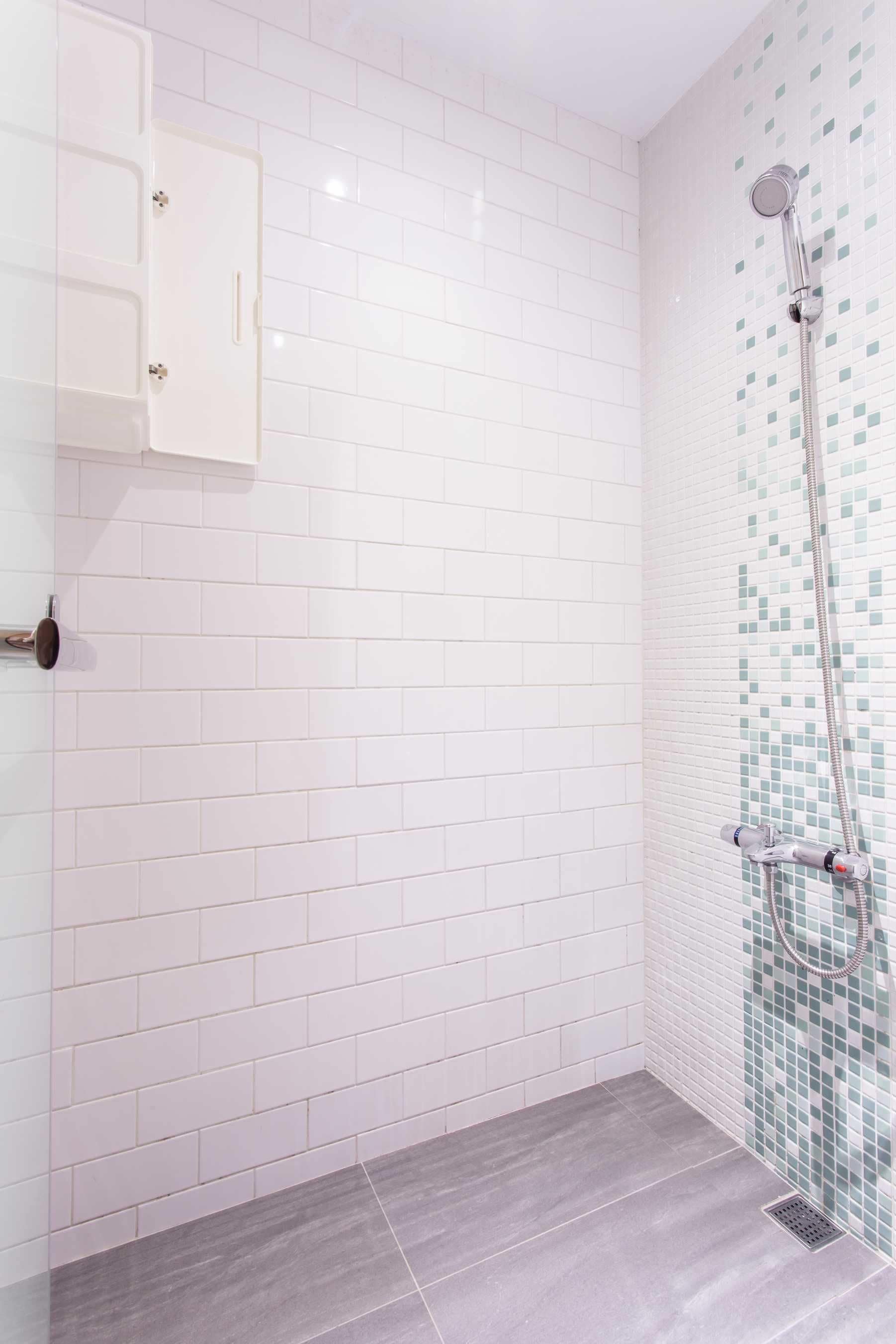A bathroom with white tiled walls, a shower with a mosaic tile accent, and a grey floor.