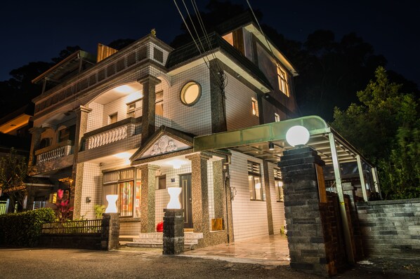 Un edificio de dos pisos con un balcón, un ventanal redondo y un área de entrada cubierta.