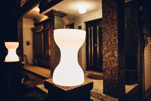 Un objeto blanco y escultórico sobre un pedestal de piedra en un pasillo tenuemente iluminado, con paredes decoradas y una puerta al fondo.
