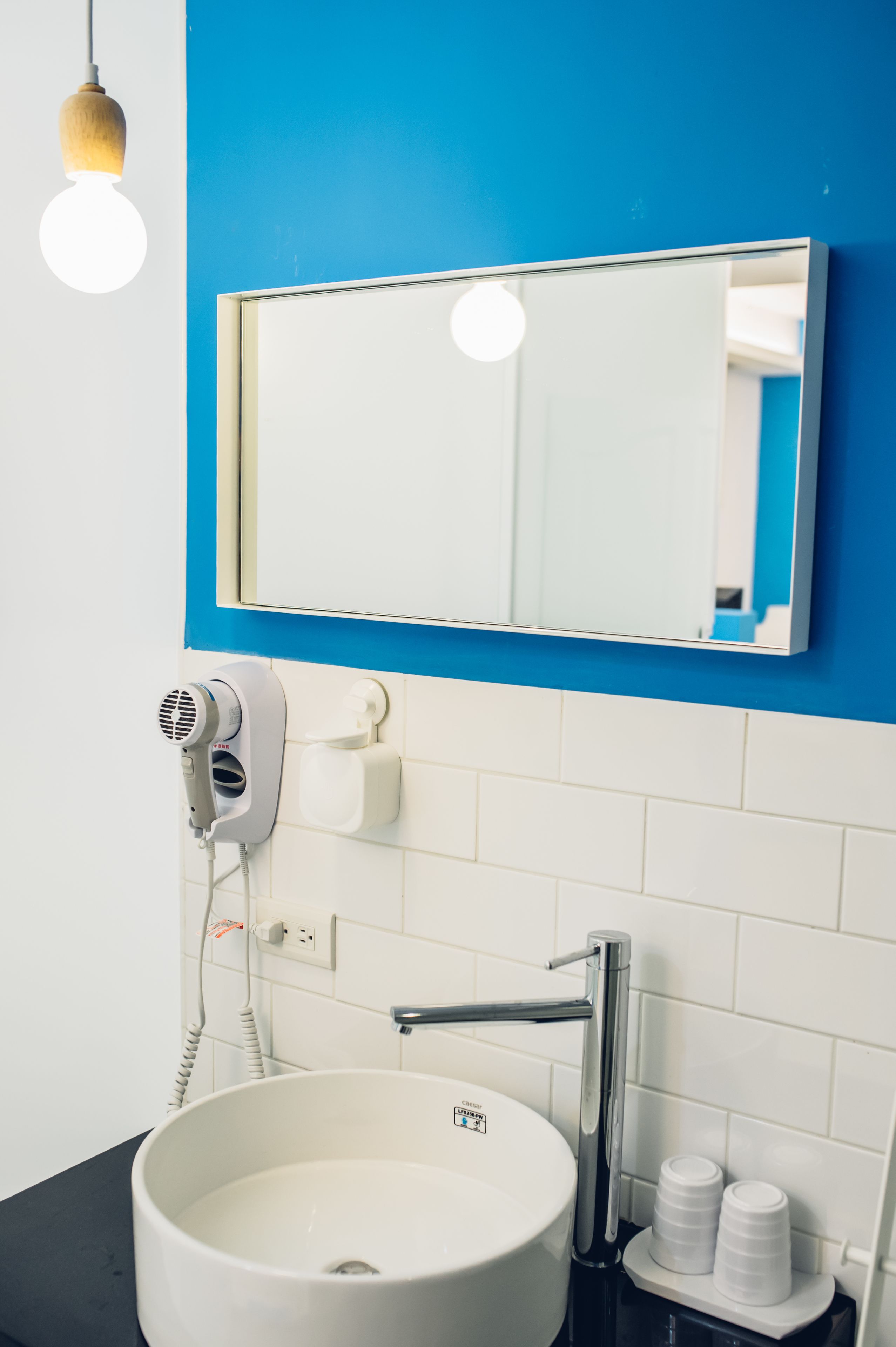 A bathroom with a white sink, a mirror, a hairdryer, and a blue wall.