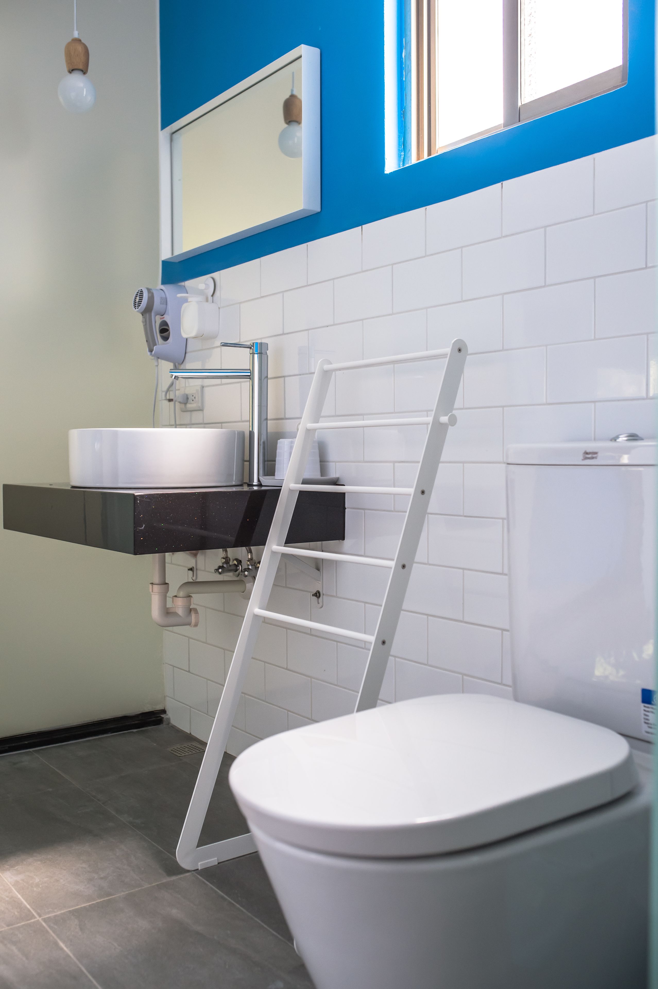 Een badkamer met een wit toilet, een wastafel met spiegel erboven en een raam met jaloezieën.