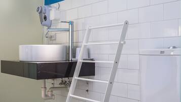 Een badkamer met een wit toilet, een wastafel met spiegel erboven en een raam met jaloezieën.