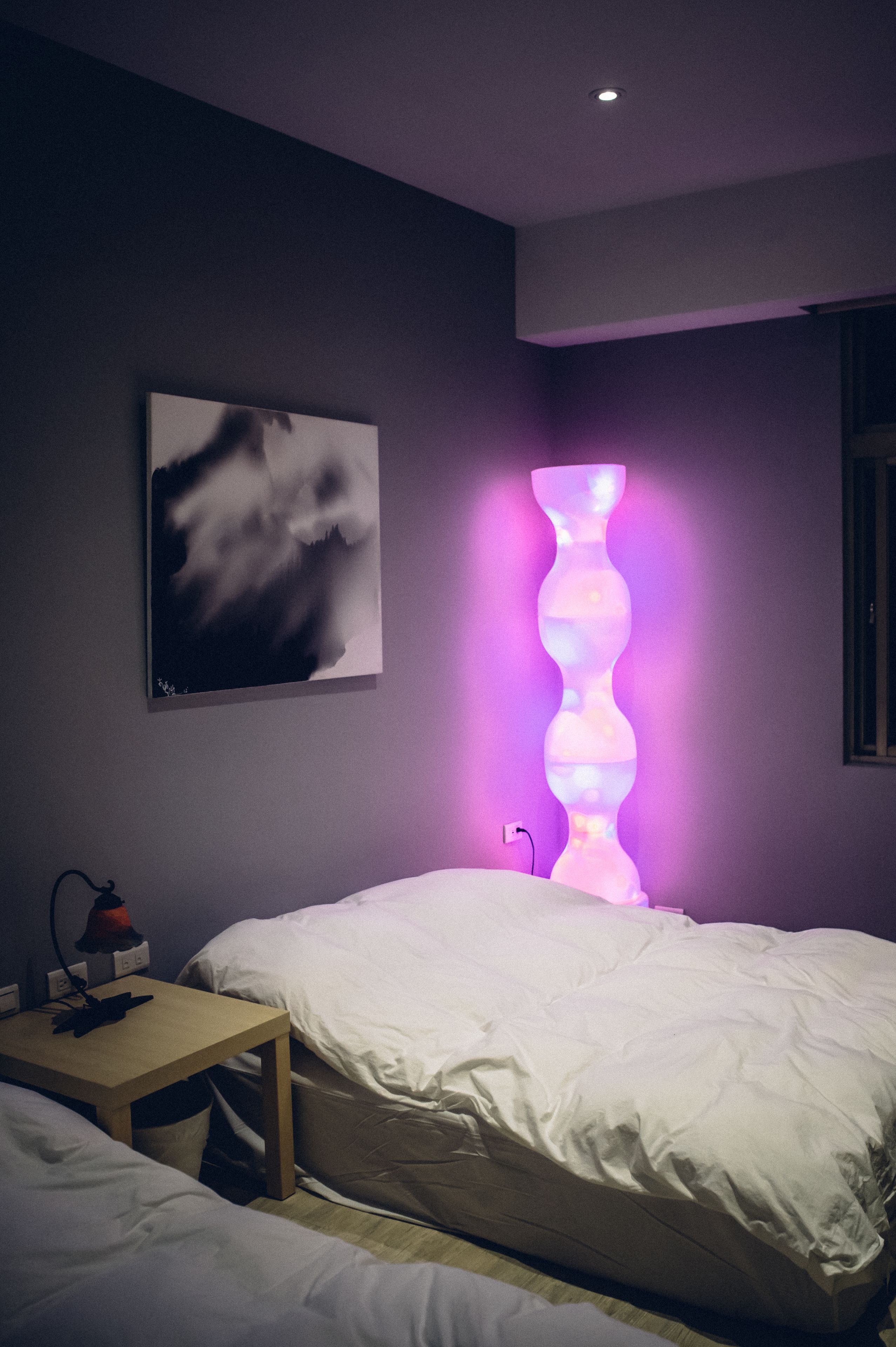A bedroom with a bed, bedside table, wall-mounted artwork, and a unique illuminated sculpture.