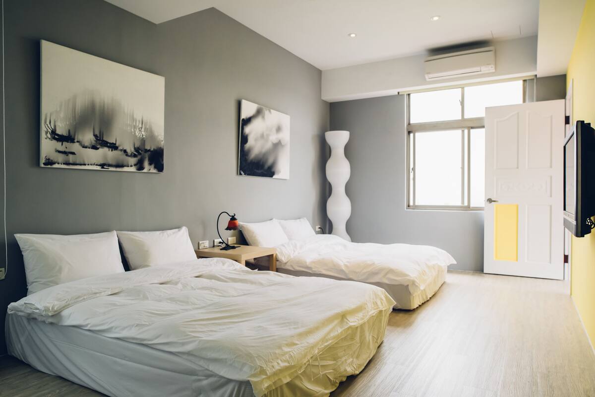 A modern bedroom with two beds, a large window, and artwork on the walls.