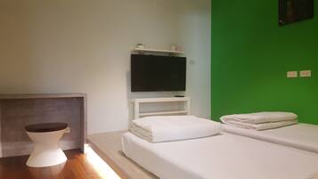 A room with a bed, a television mounted on a white shelf, a small white stool, and a green accent wall.