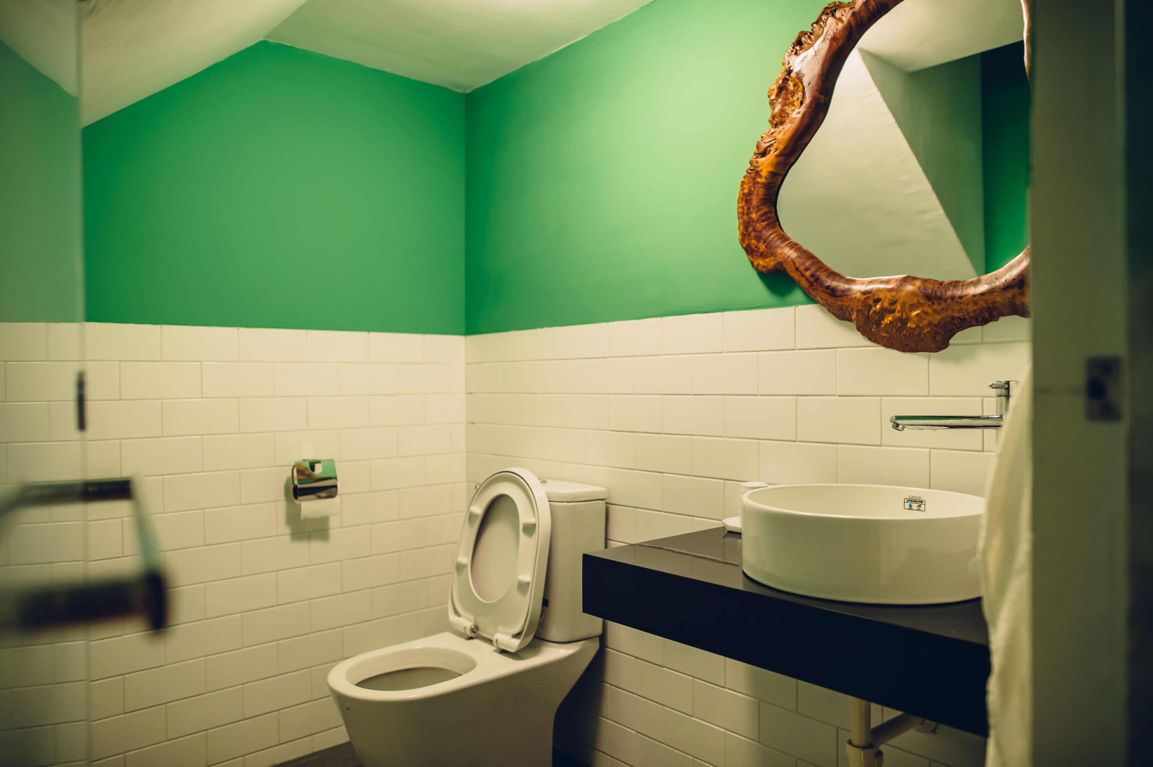A bathroom with a green wall, white tiles, a white toilet, a sink with a mirror above it, and a towel hanging on the wall.