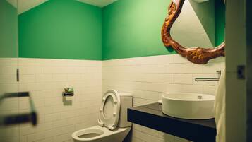 A bathroom with a green wall, white tiles, a white toilet, a sink with a mirror above it, and a towel hanging on the wall.