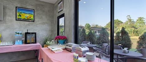 A dining area with a red and white checkered tablecloth, a buffet setup, and a view of greenery through large windows.