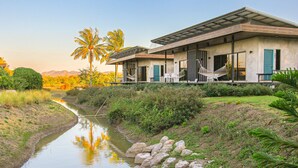 Una casa moderna con un porche cubierto, un pequeño canal de agua y una palmera.