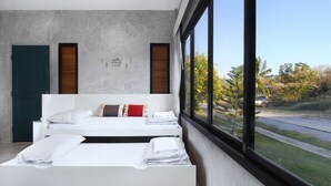 Un dormitorio moderno con un amplio ventanal, una cama con ropa de cama blanca y vistas al exterior.