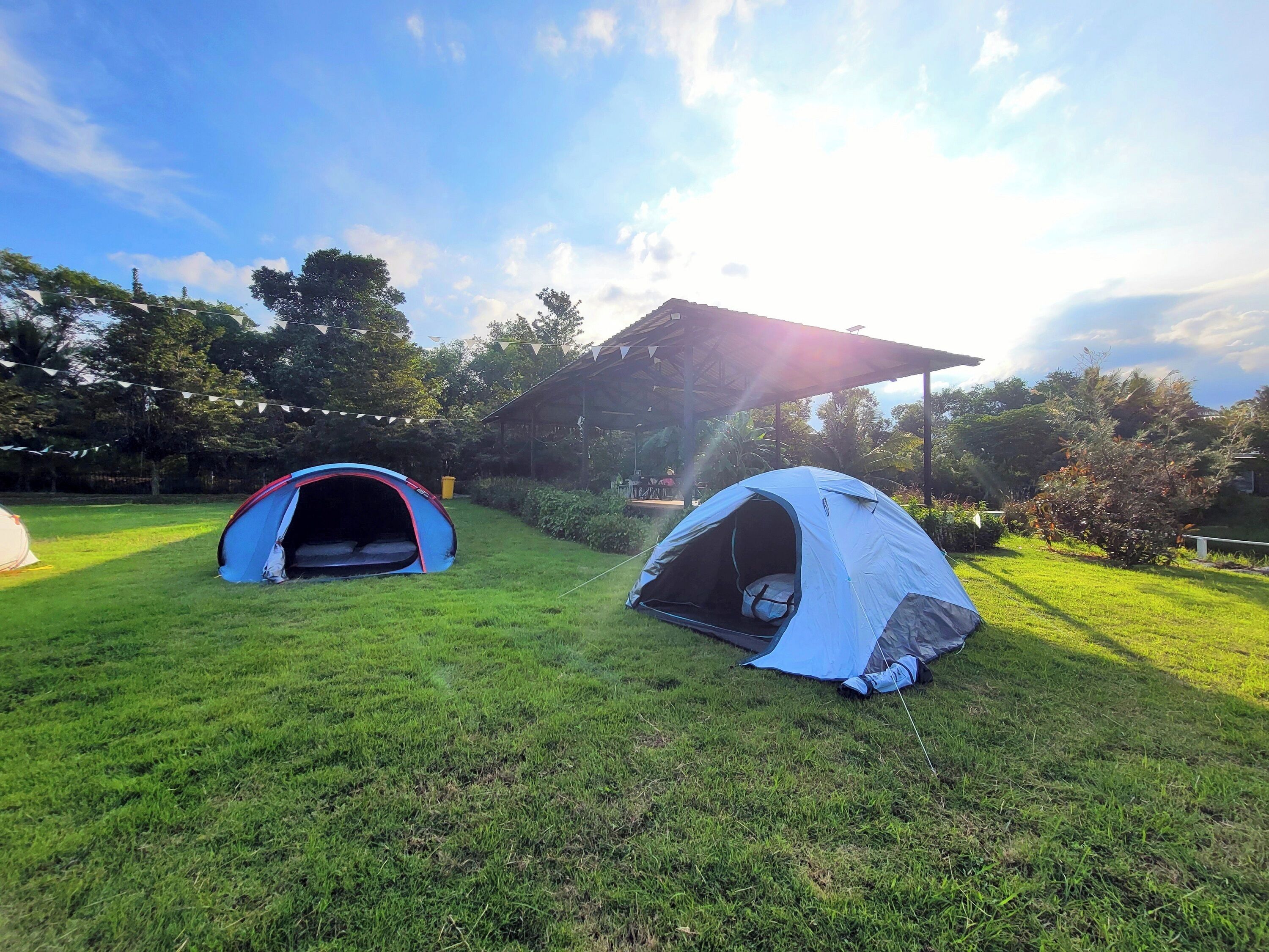 Two tents set up on a grassy field with a pavilion in the background.