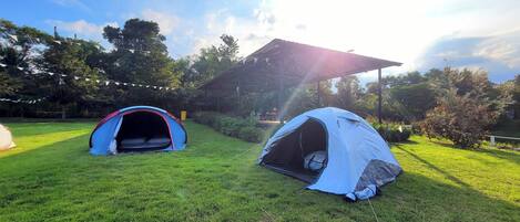 Two tents set up on a grassy field with a pavilion in the background.
