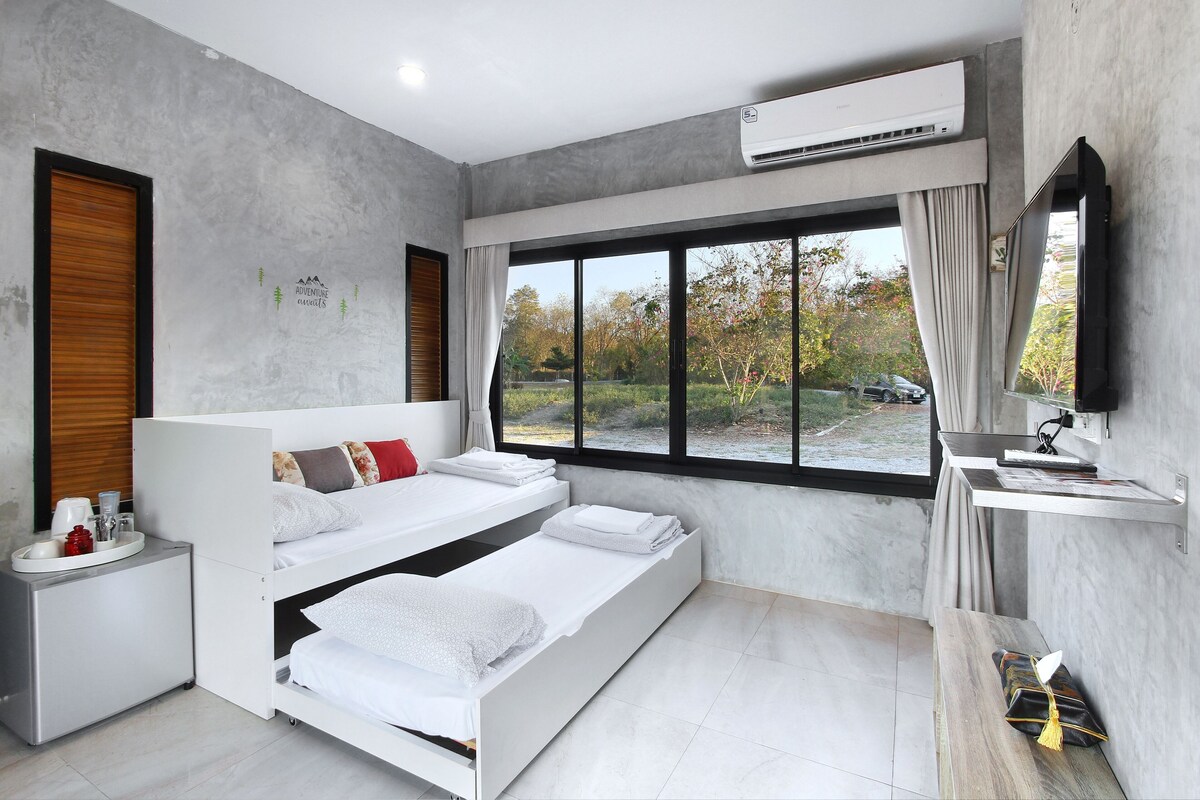 A modern bedroom with a bed, bedside tables, a vanity, and a large window with a view.