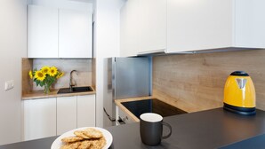 Una cocina moderna con armarios blancos, encimera de madera, un fregadero, una estufa, un hervidor amarillo y un plato de galletas.