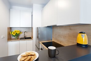 Eine moderne Küche mit weißen Schränken, einer Holz Arbeitsplatte, einer Spüle, einem Herd und einem gelben Wasserkocher, sowie einem Teller mit Keksen.