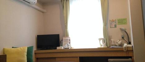 Habitación de hotel con cama, escritorio con televisor, refrigerador pequeño y ventana con cortinas.
