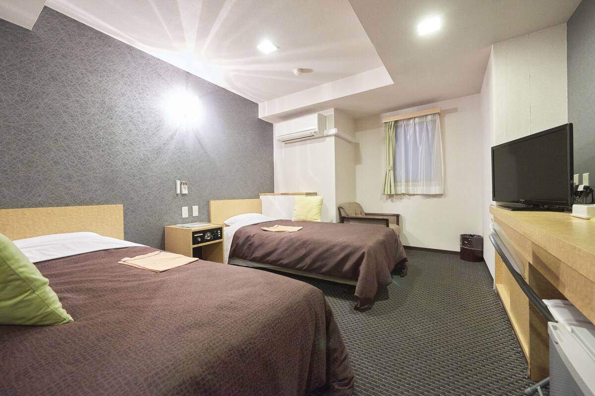 Een hotelkamer met twee bedden, een bureau, een flatscreen televisie, een stoel, een airconditioning en een raam met gordijnen.