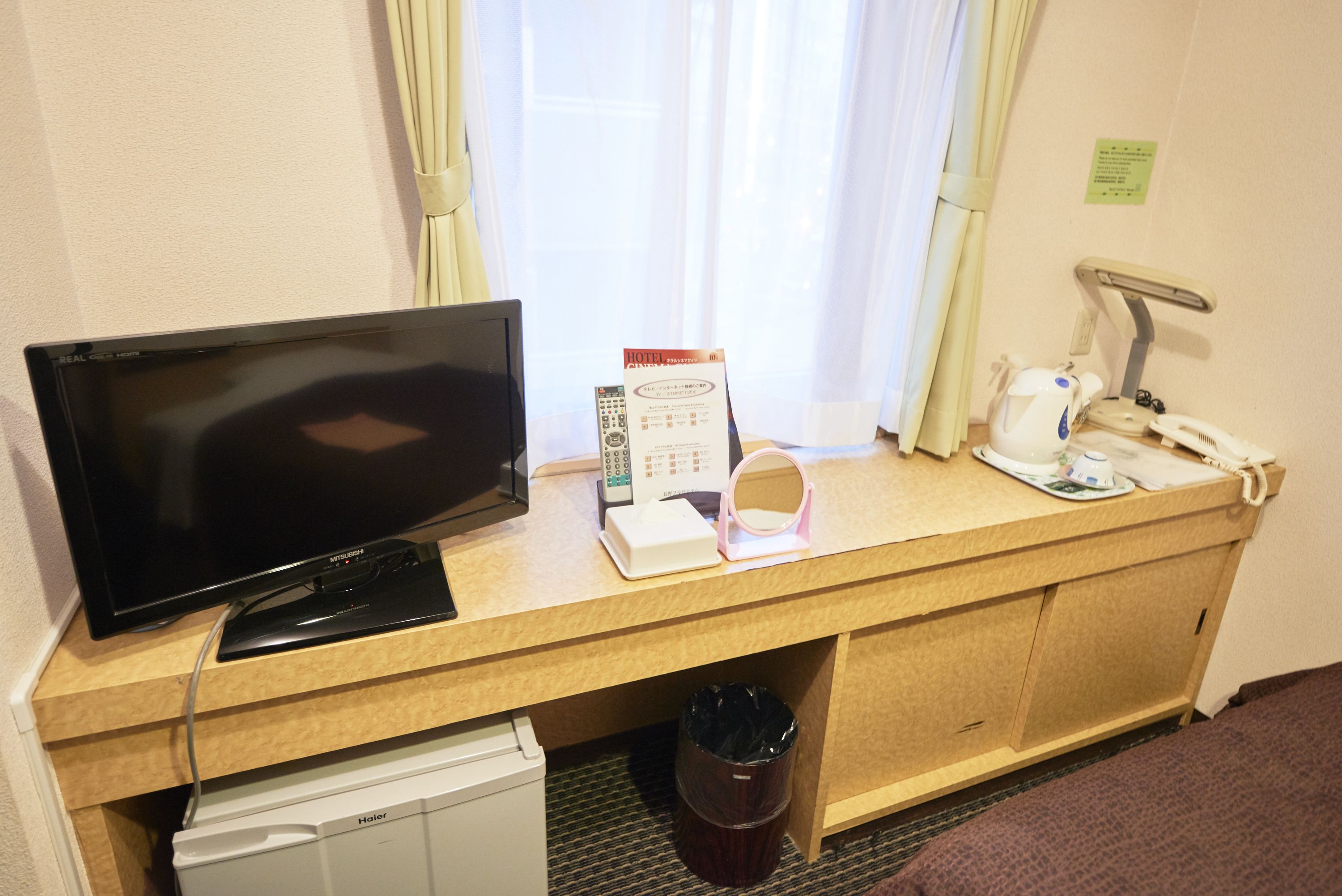A hotel room with a television, a desk with a telephone, a coffee maker, and a trash bin.