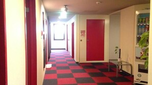 Un couloir d’hôtel avec un sol à carreaux rouges et noirs, un distributeur automatique et une porte dotée d’un panneau rouge.