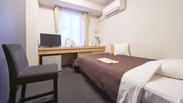 Une chambre d’hôtel avec un lit, un bureau avec un ordinateur, une chaise et une fenêtre avec des rideaux.