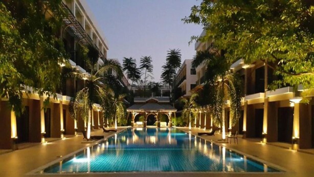 A swimming pool with a covered pavilion in the center, surrounded by palm trees and buildings with warm lighting. - Summer Tree Hotel (Bangkok)