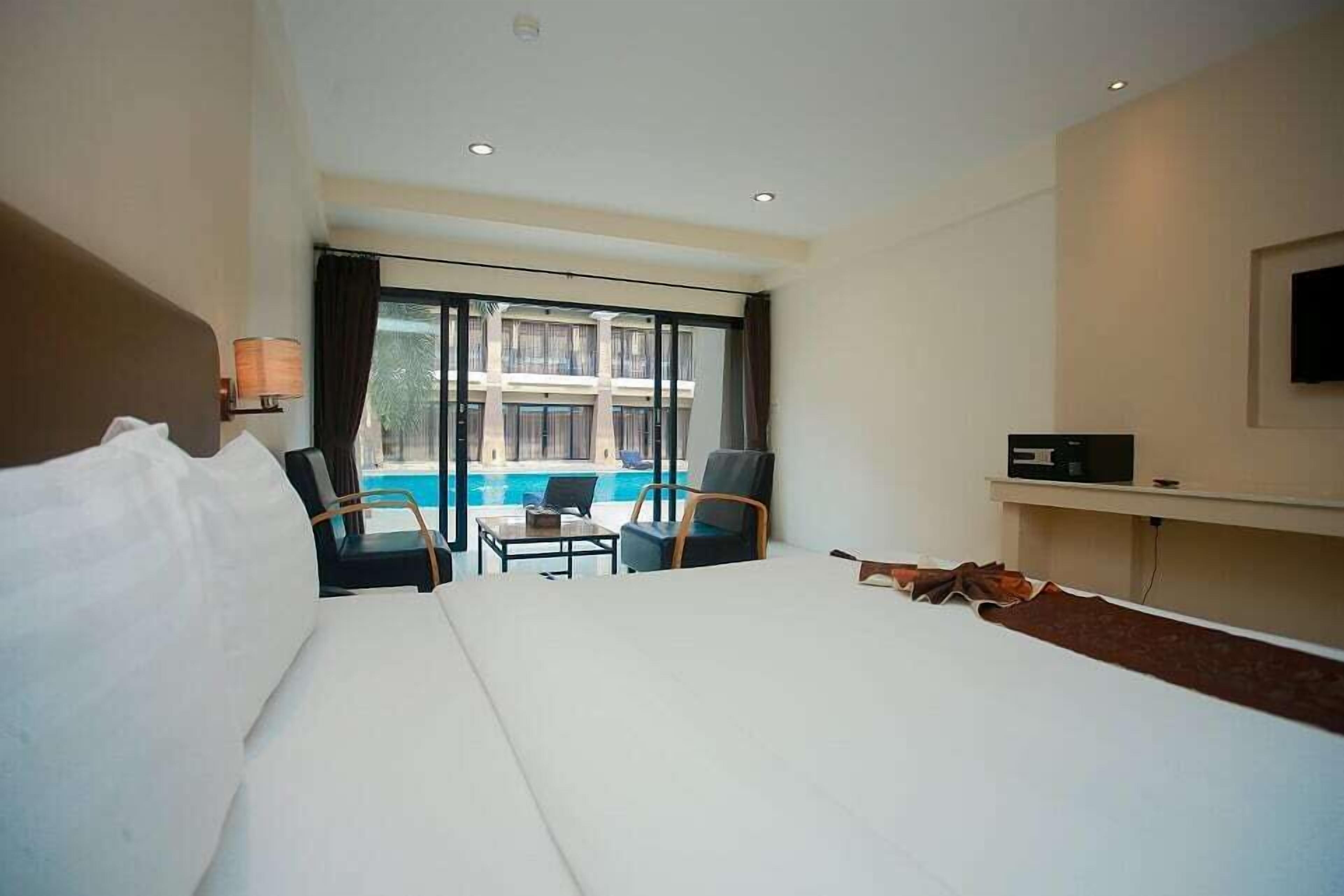 A hotel room with a large bed, a desk, a chair, a TV, and a view of a swimming pool.