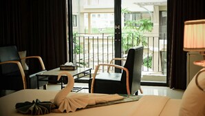 A hotel room with a bed, a desk, a chair, a lamp, and a balcony with a view of the outside. - Summer Tree Hotel (Bangkok)