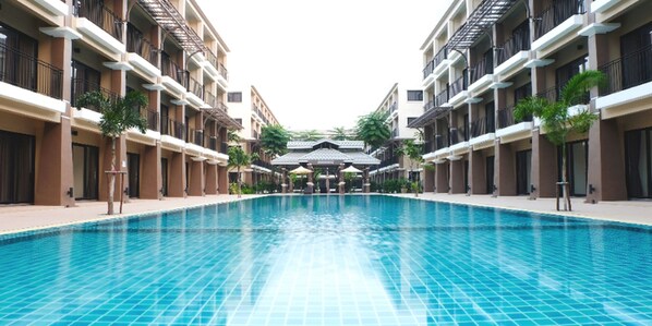 A swimming pool surrounded by multi-story buildings with balconies and outdoor seating areas.
