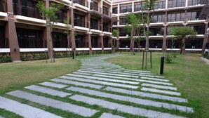 A courtyard with a stone pathway, surrounded by greenery and modern buildings with balconies. - Summer Tree Hotel (Bangkok)