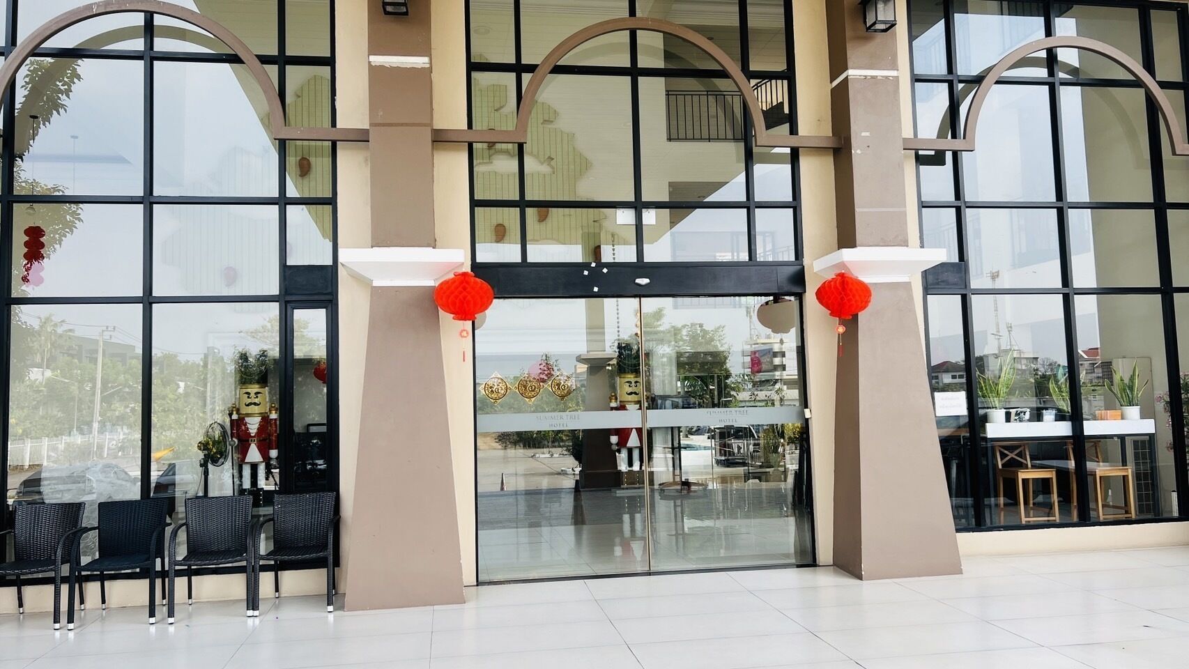 A hotel entrance with large glass doors, a reception desk, and a seating area with chairs.