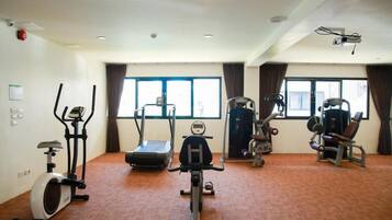 Une salle de sport équipée de machines de cardio, de matériel d’entraînement en force et dotée de grandes fenêtres.