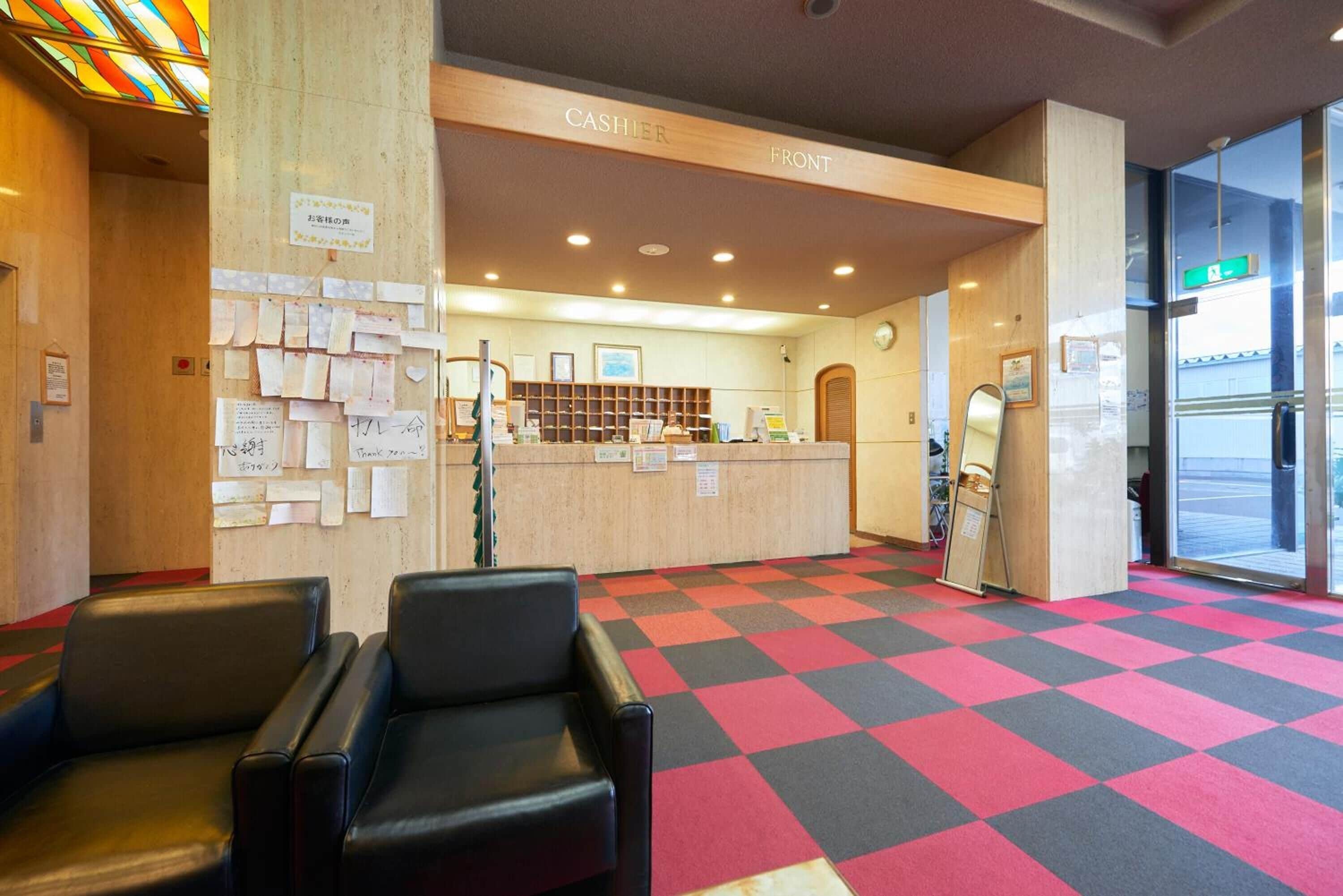 A hotel reception area with a check-in counter, a bulletin board with notes, and a seating area with chairs.