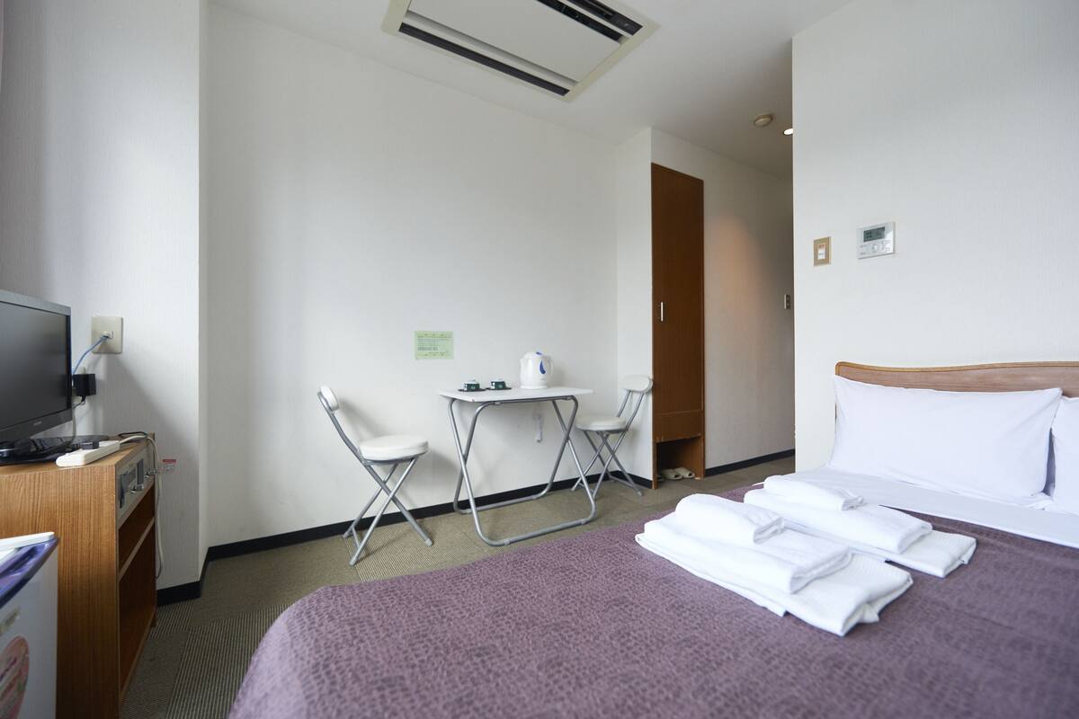 A hotel room with a bed, a desk with a chair, a television, and a small table with a chair.