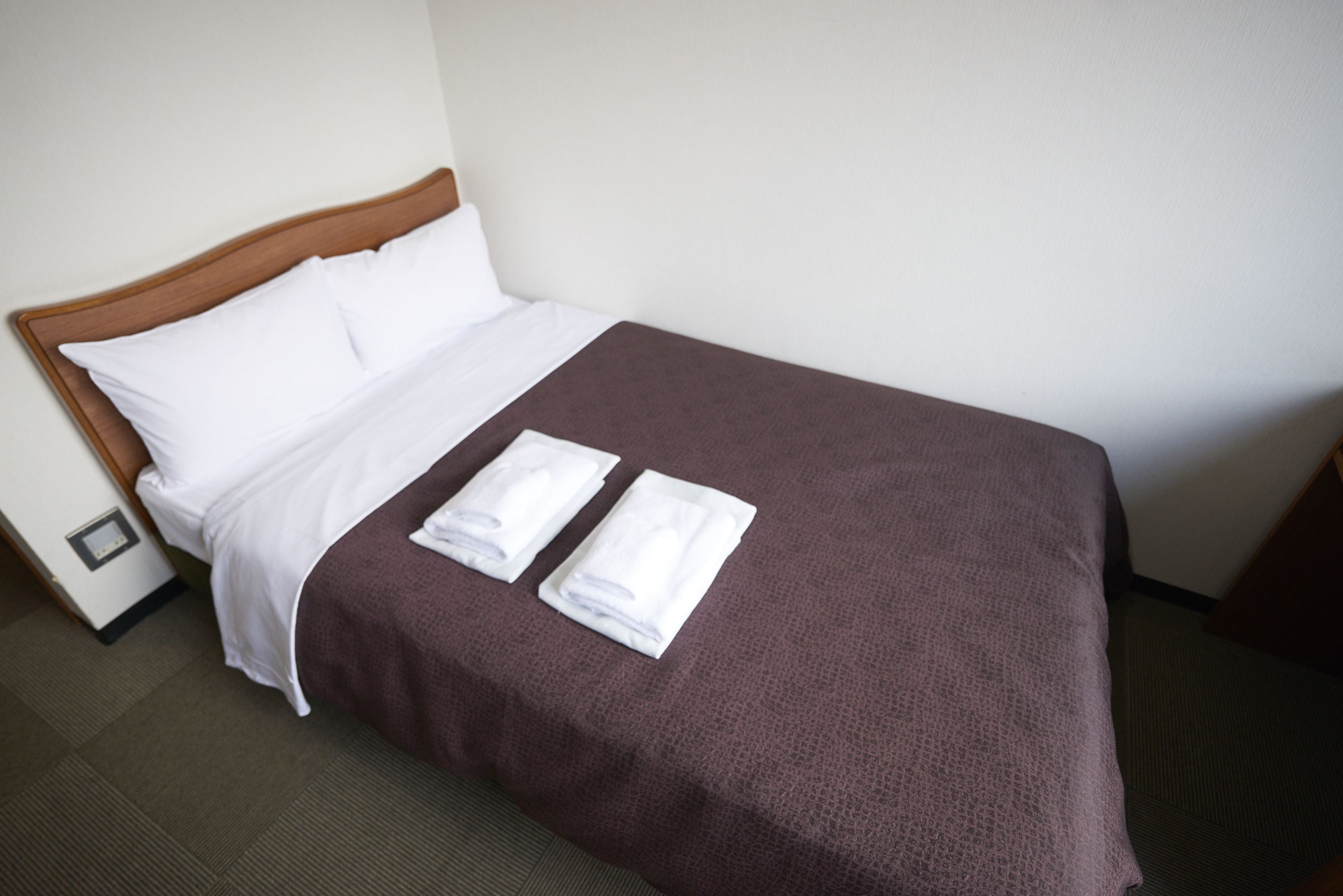 A neatly made bed with a brown cover, white pillows, and two folded white towels on the bed.