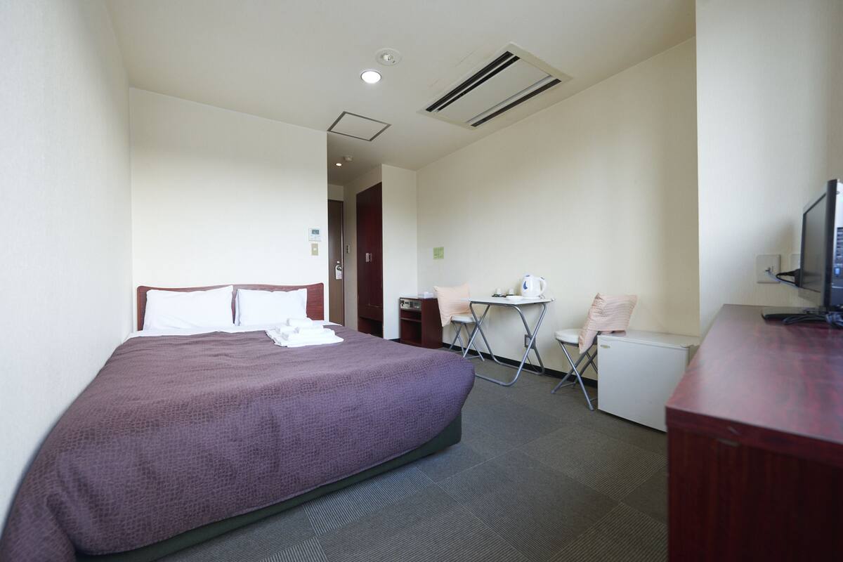 Habitación de hotel con cama, escritorio, silla, refrigerador pequeño y televisor.