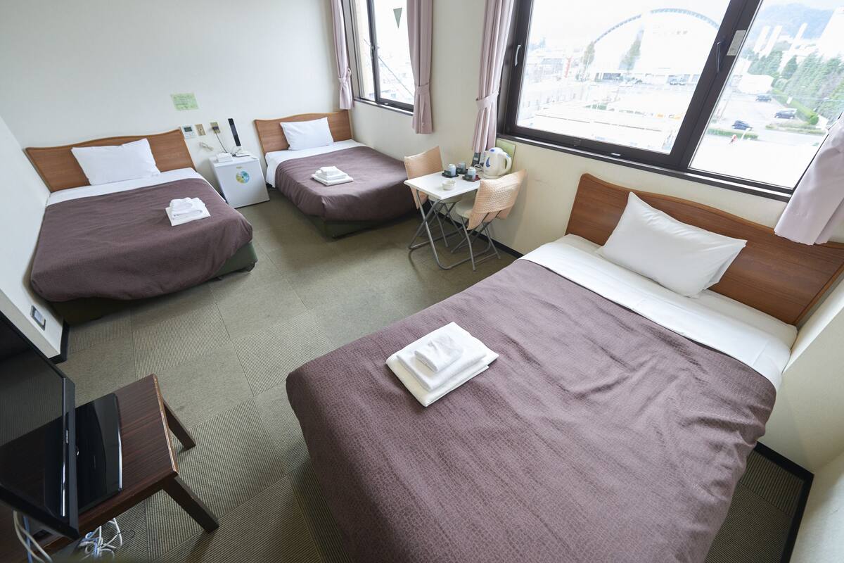 Una habitación de hotel con dos camas individuales, una cama doble, una pequeña mesa con sillas y un escritorio con una computadora.