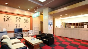 Eine Hotelhalle mit Empfangsschalter, einer Sitzgelegenheit und einer großen Wand mit japanischer Kalligraphie.