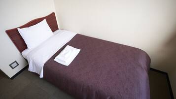 A neatly made bed with a brown cover and white linens, a power outlet on the wall, and a dark carpeted floor.
