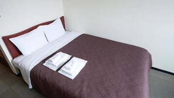 Een net opgemaakt bed met witte lakens en een bruine deken, samen met opgevouwen witte handdoeken.