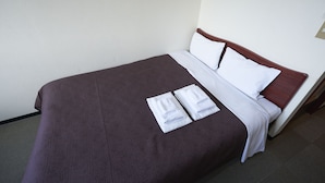 Ein ordentlich bezogenes Bett mit einer braunen Decke, weißen Kissen und zwei gefalteten weißen Handtüchern.