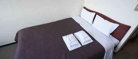 A neatly made bed with a brown cover, white pillows, and two folded white towels on the bed.