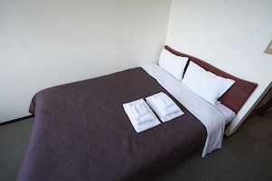 Una cama bien hecha con una cubierta marrón, almohadas blancas y dos toallas blancas dobladas sobre la cama.