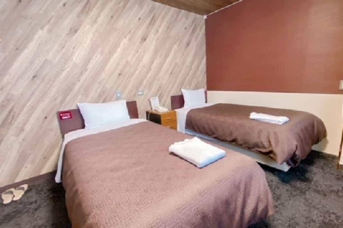 A hotel room with two beds, a wooden accent wall, a brick wall, and a carpeted floor.